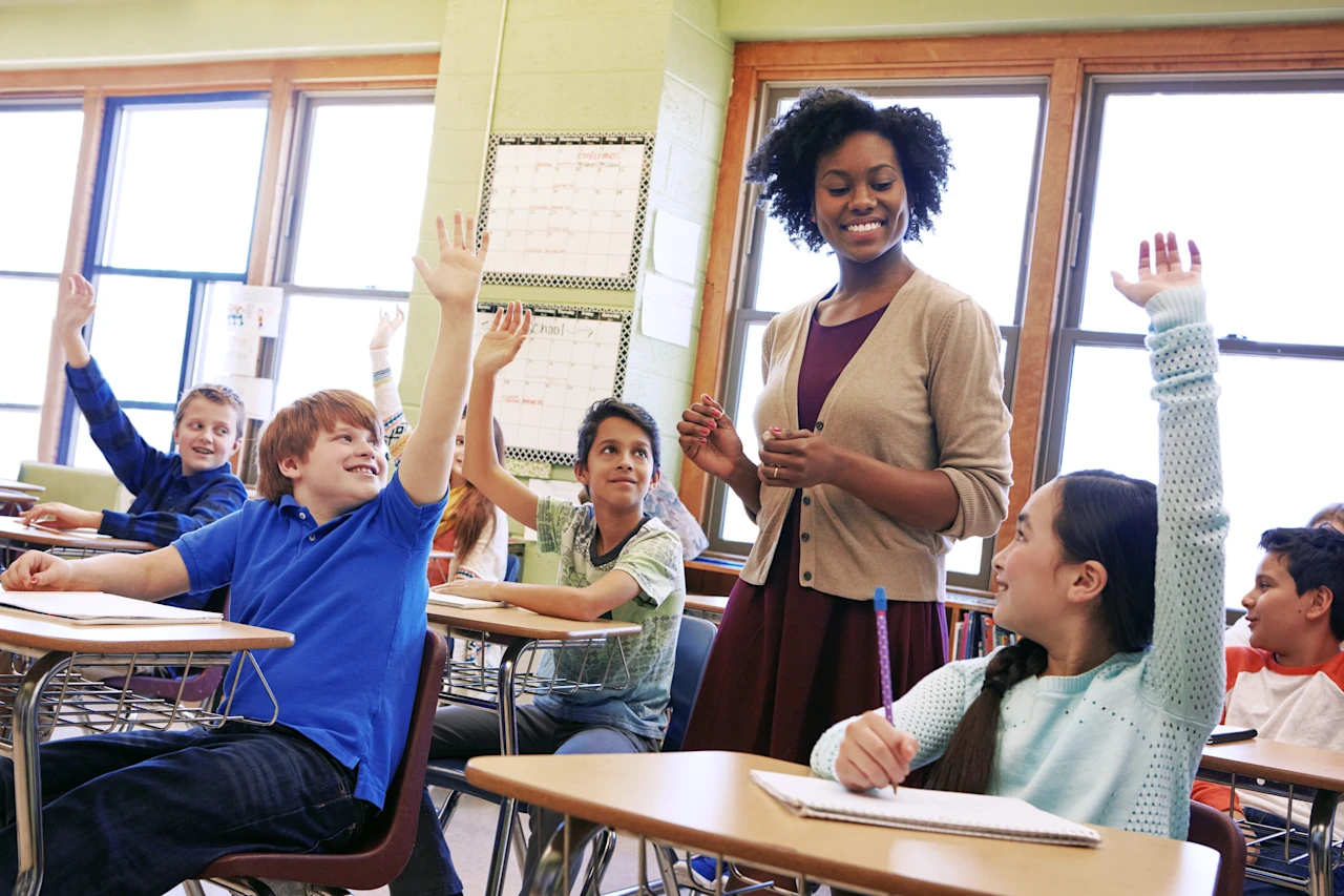 Female teacher in classroom with children hands up