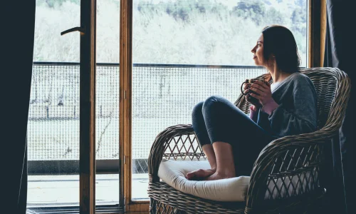 Winter wellness blog image 23/11/24 - woman looking out of window with mug